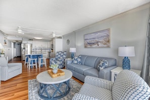 A spacious living area with a sofa, armchairs, a coffee table, and a kitchen in the background. - Royal Garden 1115 - 2 Bed 2 Bath Luxury Condo with Ocean and Marsh Views! (Garden City Beach)