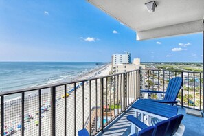 A balcony with a view of a beach and ocean, featuring a pool table and chairs. - Royal Garden 1115 - 2 Bed 2 Bath Luxury Condo with Ocean and Marsh Views! (Garden City Beach)