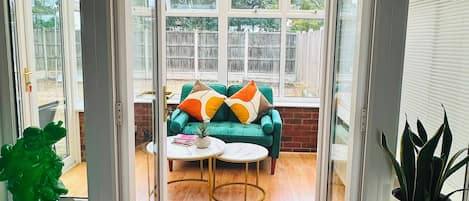 A conservatory with a green sofa, two round tables, and a ceiling fan.