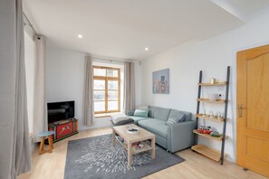 Un salon moderne avec un canapé, une table basse, un téléviseur et une fenêtre avec des rideaux.