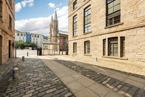 A cobblestone street with historic buildings, a church with a tall spire, and a bus stop. - Historic Whisky Bond 2BR | Free Parking - Pass the Keys (Edinburgh)