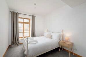 Une chambre à coucher avec un lit, une table de chevet, une lampe et une fenêtre avec des rideaux.