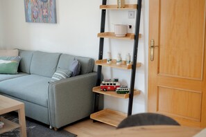 A living room with a grey sofa, a wooden shelf unit with decorative items, and a wooden door. - Historic Whisky Bond 2BR | Free Parking - Pass the Keys (Edinburgh)