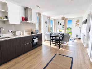 A modern kitchen with a dining area, large windows, and a view of the outdoors. - Top Floor Flat With Balcony Overlooking Manchester - Pass the Keys (Salford)