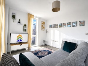 Ein modernes Wohnzimmer mit einer Couch, einem Fernseher, einer Heizung und einem Fenster mit Vorhängen.