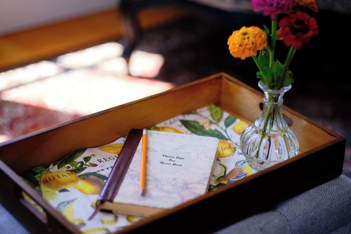 Une boîte en bois ornée d’un motif floral, contenant un livre d’or, un crayon et un vase transparent rempli de fleurs.