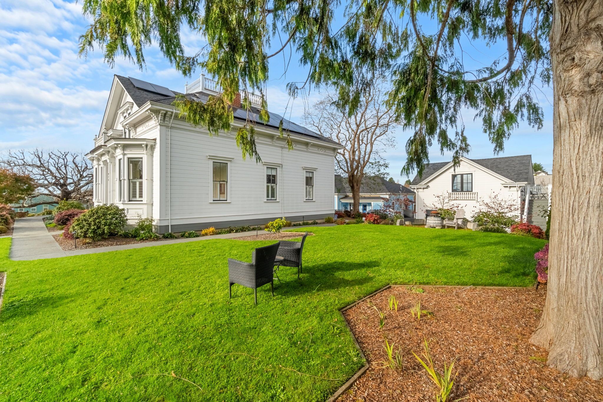 A white two-story house with a front lawn, a bench, and a tree.