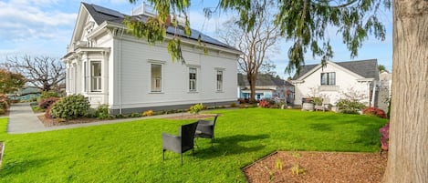 A white two-story house with a front lawn, a bench, and a tree.