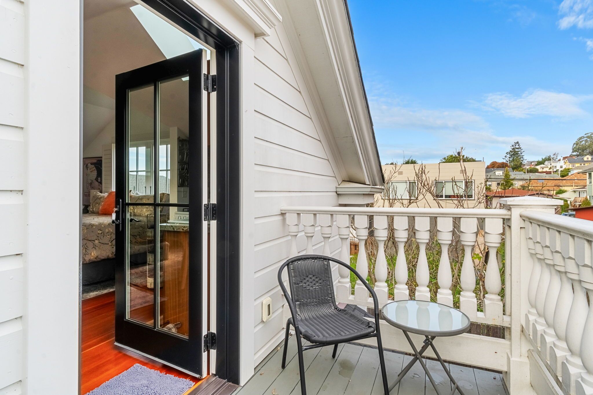 A balcony with a glass door leading to a room, a chair, and a small table.