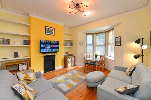 A living room with a fireplace, a television mounted on the wall, and a dining area with a table and chairs. - Charming Apartment in the Heart of Llandaff - Pass the Keys (Cardiff)
