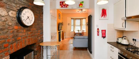 A kitchen with a brick wall, a clock, pendant lights, and a dining area with a sofa.