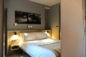 A hotel room with a bed, bedside lamps, a nightstand, a wall-mounted thermostat, and a painting of a tree. - Charming Apartment in the Heart of Llandaff - Pass the Keys (Cardiff)