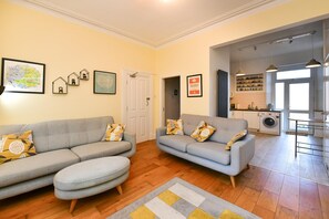 A living room with two grey sofas and a patterned rug, a kitchen with a washing machine, and a dining area with pendant lights. - Charming Apartment in the Heart of Llandaff - Pass the Keys (Cardiff)