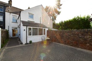 Ein Wohnhaus mit befestigter Auffahrt, einer Steinmauer und einer kleinen Terrasse mit Sitzgelegenheit.