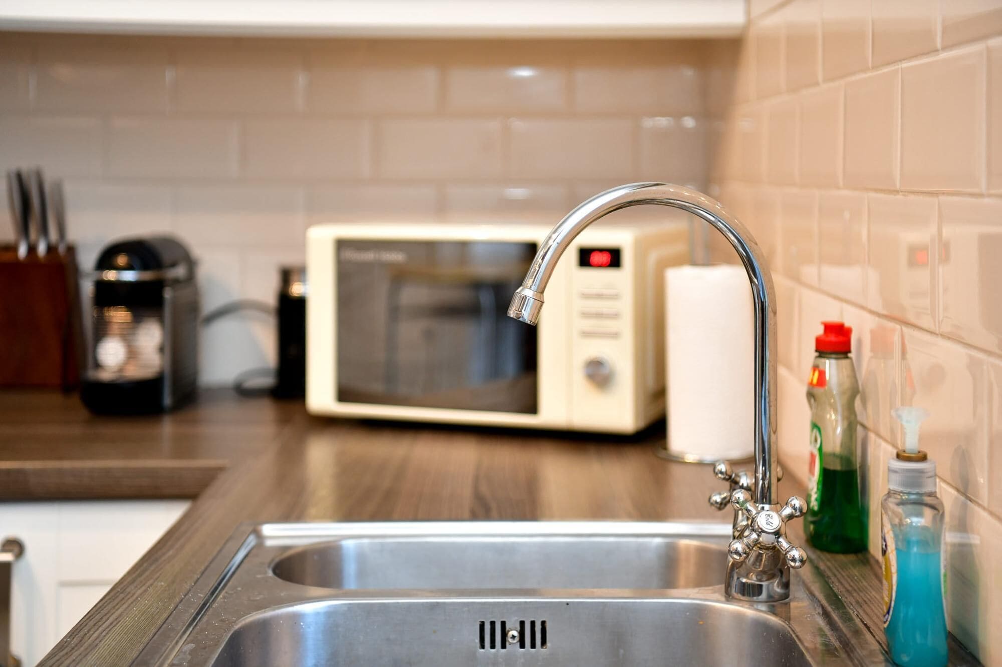 A kitchen with a stainless steel sink, a microwave, and a faucet with a red handle.