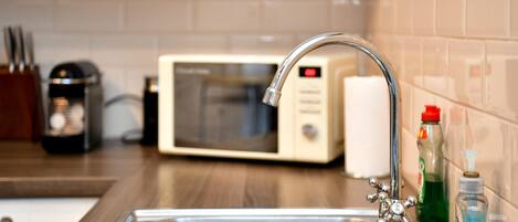 A kitchen with a stainless steel sink, a microwave, and a faucet with a red handle.