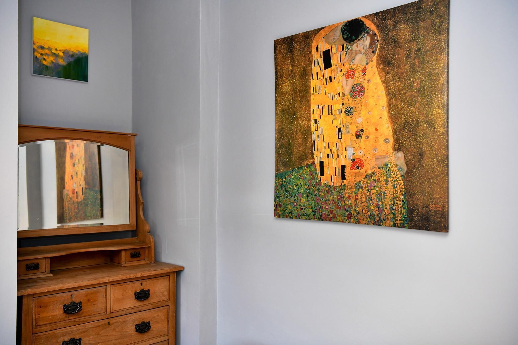 A room with a wooden dresser, a framed painting of a couple, and a smaller painting above the dresser.