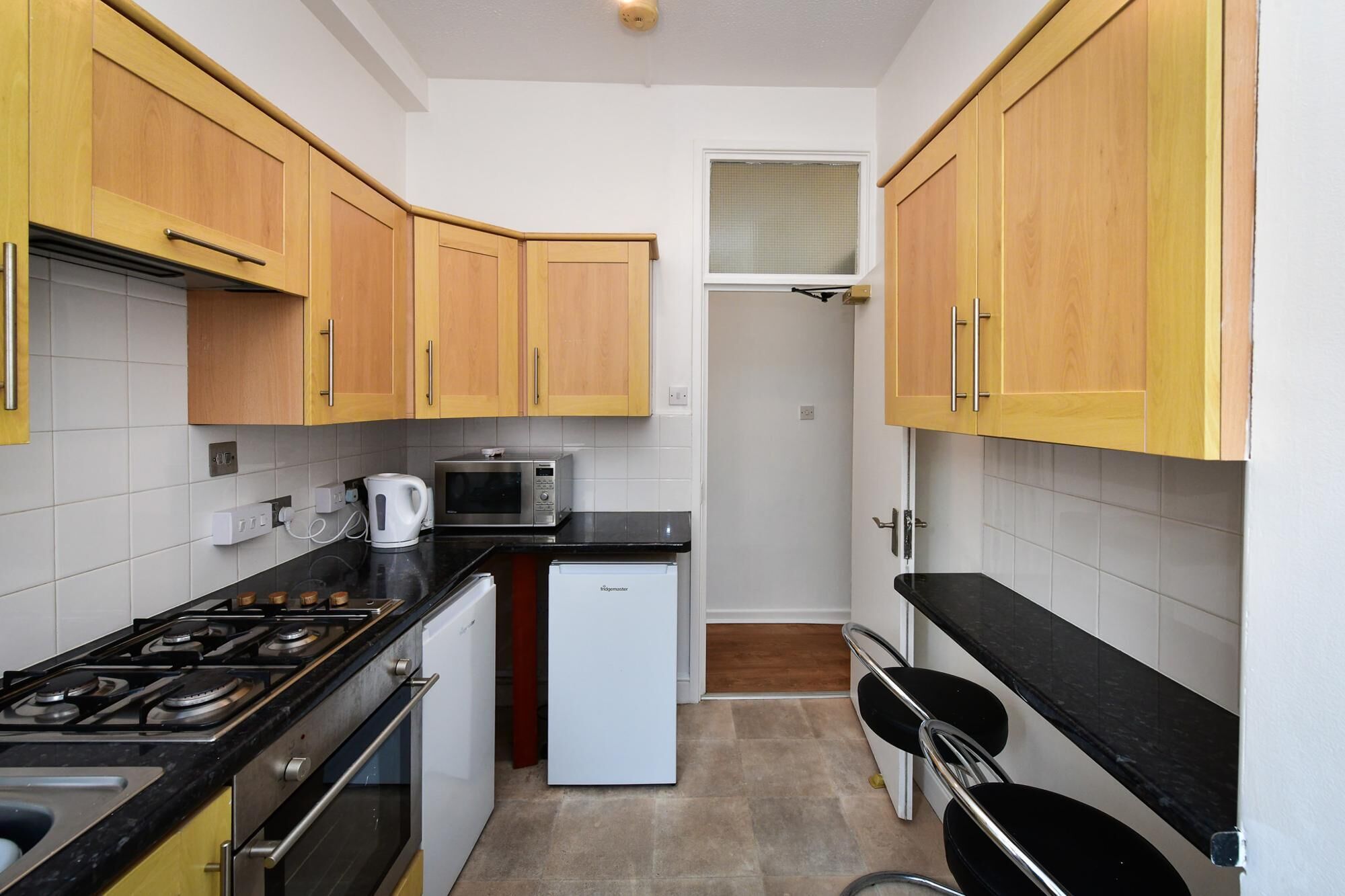 A compact kitchen with wooden cabinets, a gas stove, a microwave, and a small refrigerator.