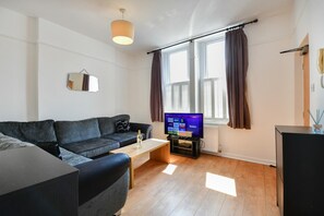 A living room with a sofa, a coffee table, a flat-screen TV, and a window with curtains. - Spacious Cardiff Apartment | WiFi | Near City - Pass the Keys (Cardiff)