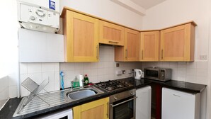 A compact kitchen with wooden cabinets, a gas stove, a microwave, a dishwasher, and a refrigerator. - Spacious Cardiff Apartment | WiFi | Near City - Pass the Keys (Cardiff)