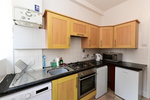 A compact kitchen with wooden cabinets, a gas stove, a microwave, a dishwasher, and a refrigerator. - Spacious Cardiff Apartment | WiFi | Near City - Pass the Keys (Cardiff)