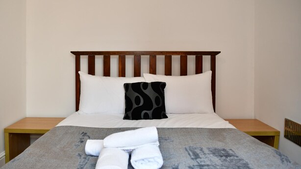 A bed with white linens, a black patterned pillow, and rolled towels on a grey blanket. - Spacious Cardiff Apartment | WiFi | Near City - Pass the Keys (Cardiff)