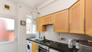 A compact kitchen with a washing machine, oven, and a small refrigerator. - Spacious Cardiff Apartment | WiFi | Near City - Pass the Keys (Cardiff)