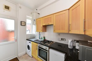 A compact kitchen with a washing machine, oven, and a small refrigerator. - Spacious Cardiff Apartment | WiFi | Near City - Pass the Keys (Cardiff)