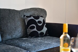 A grey sofa with a black and white patterned pillow. A bottle and a glass are on the sofa. - Spacious Cardiff Apartment | WiFi | Near City - Pass the Keys (Cardiff)