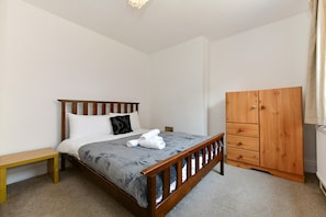 A bedroom with a wooden bed, a wooden wardrobe, a bench, and a radiator. - Spacious Cardiff Apartment | WiFi | Near City - Pass the Keys (Cardiff)
