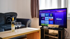 A living room with a television displaying the Roku interface, a bottle of wine, and two glasses on a wooden table. - Spacious Cardiff Apartment | WiFi | Near City - Pass the Keys (Cardiff)