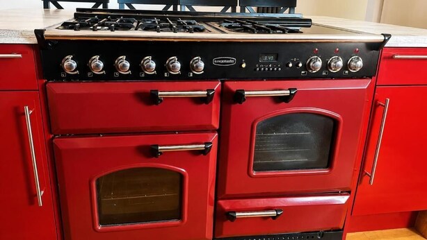 Una cocina roja con estufa a gas, dos hornos y un refrigerador rojo.