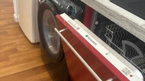Un lavadero pequeño y moderno con lavadora y secadora integradas, suelo de madera y un armario rojo.