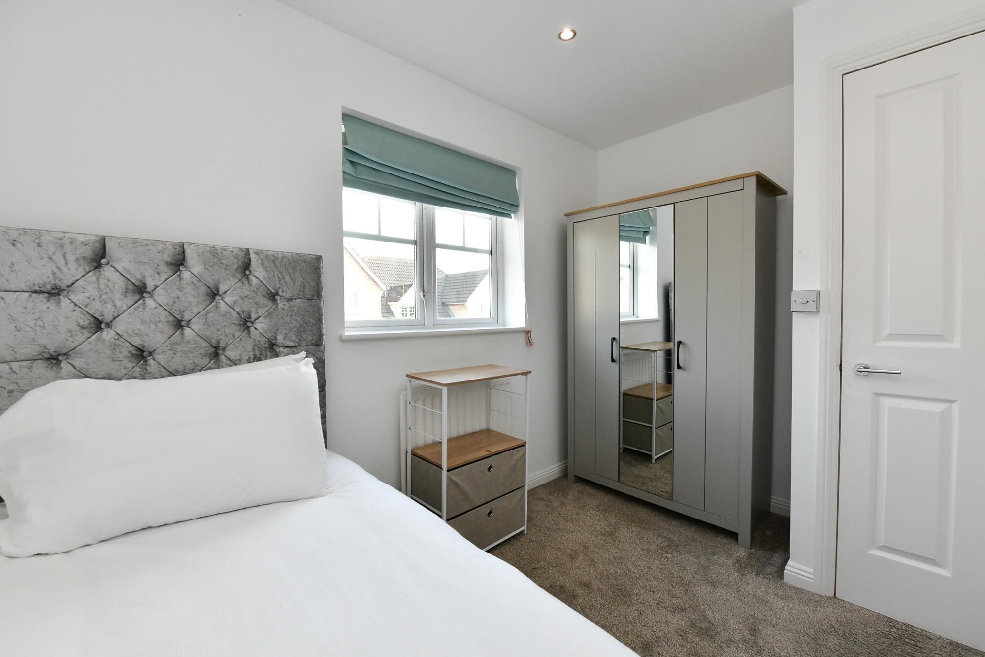 A bedroom with a bed, a wardrobe, a bedside table, and a window with curtains.