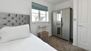 Un dormitorio con cama, armario, mesita de noche y ventana con cortinas.