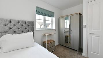A bedroom with a bed, a wardrobe, a bedside table, and a window with curtains.