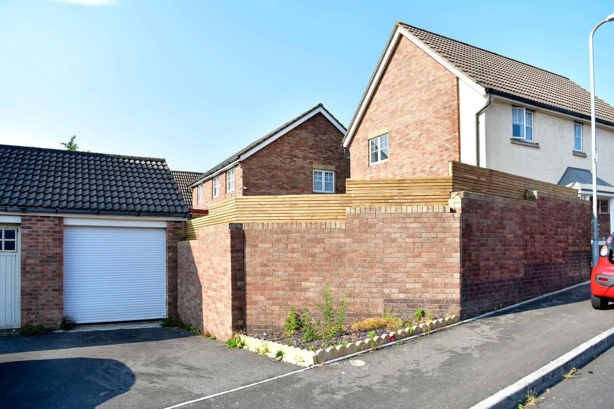 A residential building with a garage, a brick wall, and a small garden area.