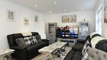 A modern living room with a black leather sofa, a marble coffee table, and a flat-screen TV mounted on the wall.