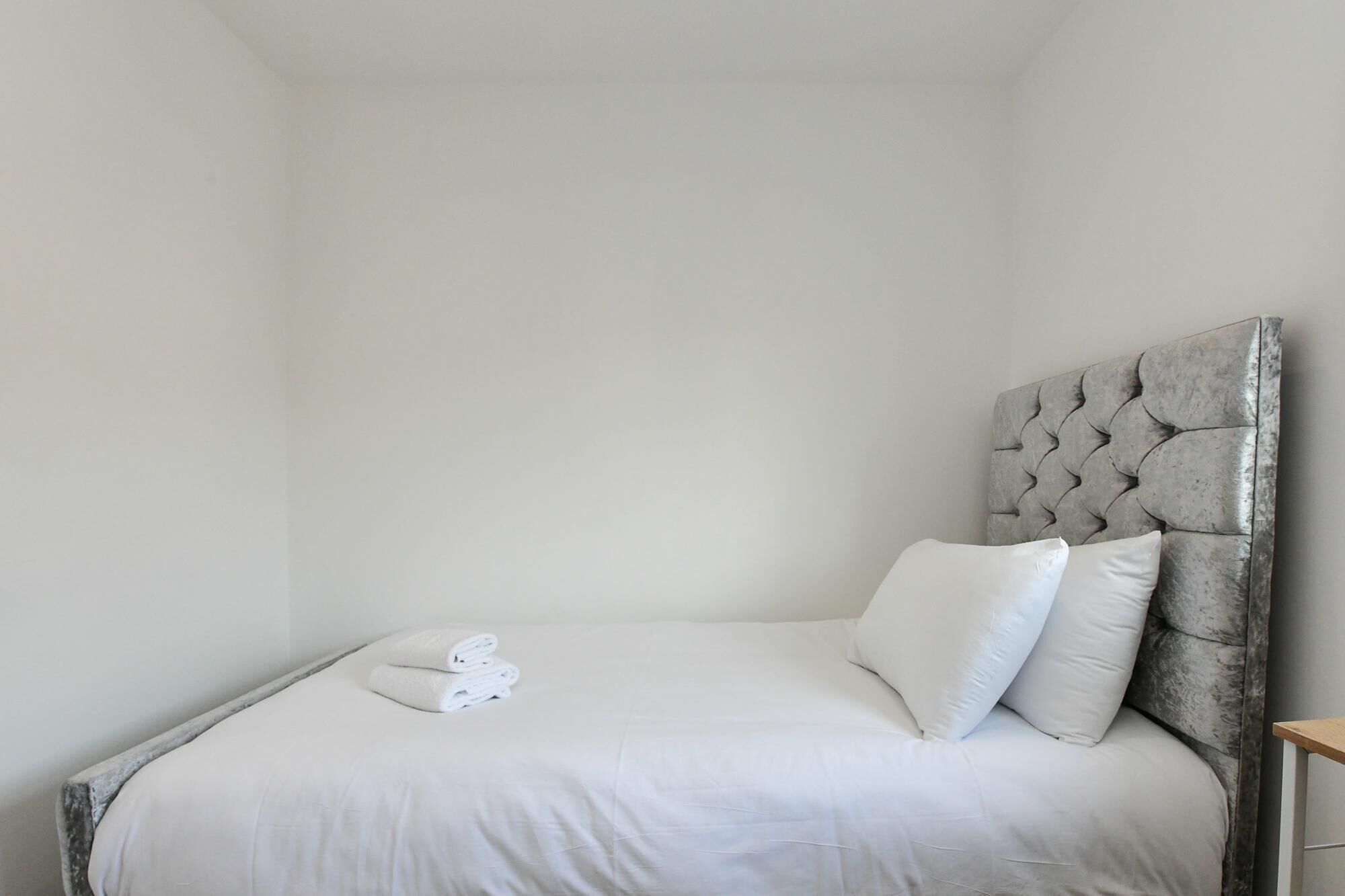 A single bed with a tufted headboard, white bedding, and a neatly folded towel.