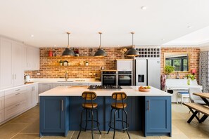 A modern kitchen with a central island, bar stools, and a brick wall backsplash. - Large & Modern 4Bed Family Home - Pass the Keys (Warwick)