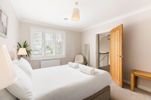 A bedroom with a bed, a bedside lamp, a window with blinds, a radiator, a chair, a wooden door, and a wooden bench. - Large & Modern 4Bed Family Home - Pass the Keys (Warwick)