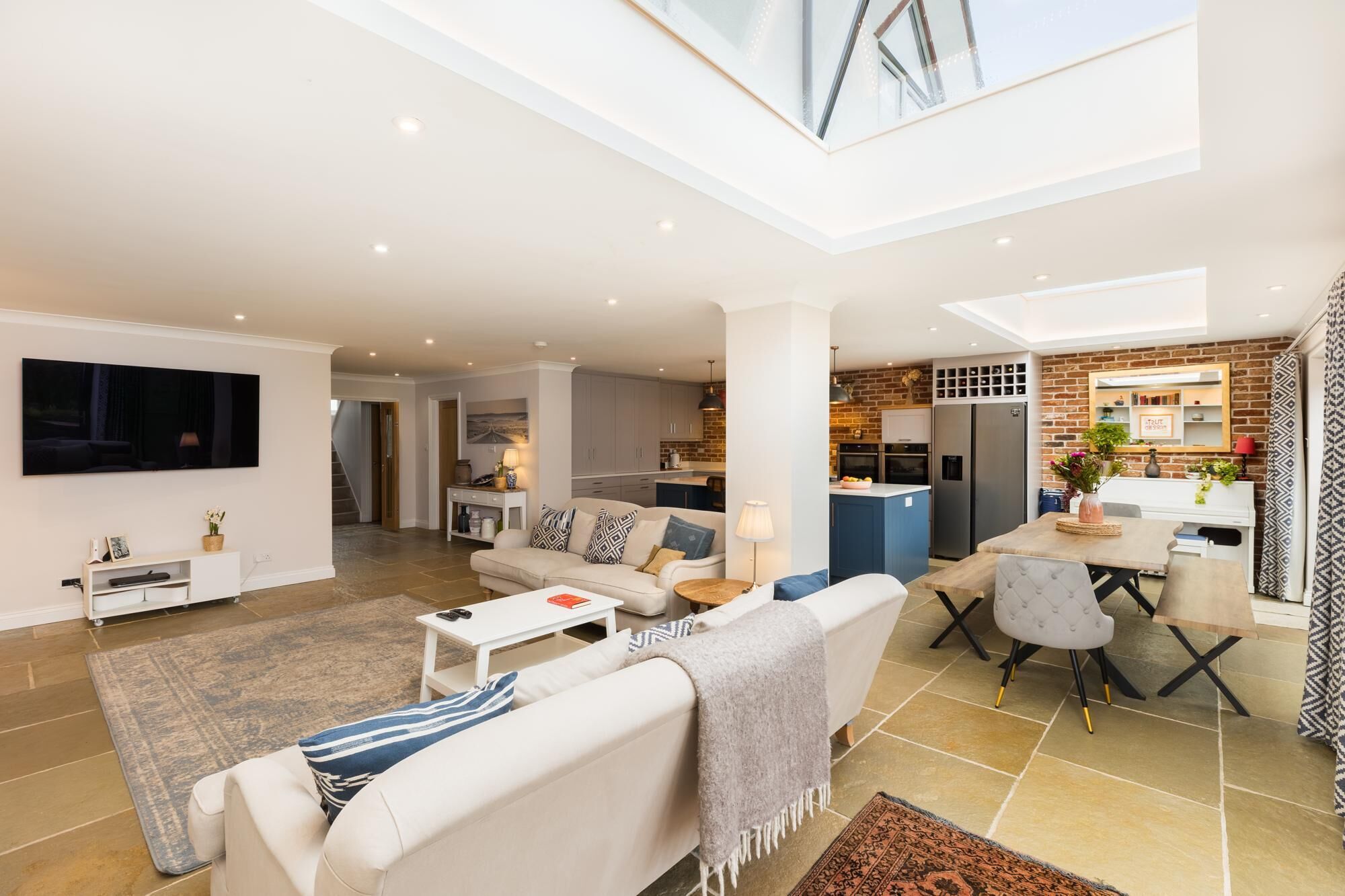 A spacious living area with a high ceiling, a dining table, and a kitchen with brick walls.