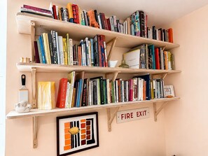Ein Bücherregal mit mehreren Einlegebögen, gefüllt mit Büchern, einem gerahmten Kunstwerk und einem Feuerschutzschild.