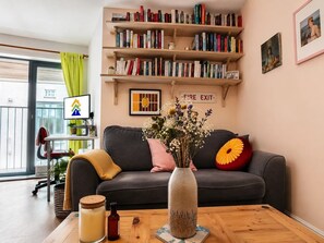 Ein Wohnzimmer mit einer Couch, einem Couchtisch, einem Bücherregal und einer Vase mit Blumen.