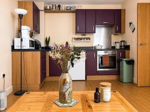 Eine moderne Küche mit violetten Schränken, einem Edelstahlkühlschrank und einem Holzessttisch mit einem Blumenstrauß.