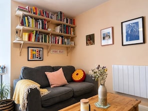 A living room with a grey sofa, a bookshelf, a vase with flowers, and a radiator. - Central Flat | Pets Allowed | 5 Min From Deansgate - Pass the Keys (Manchester)