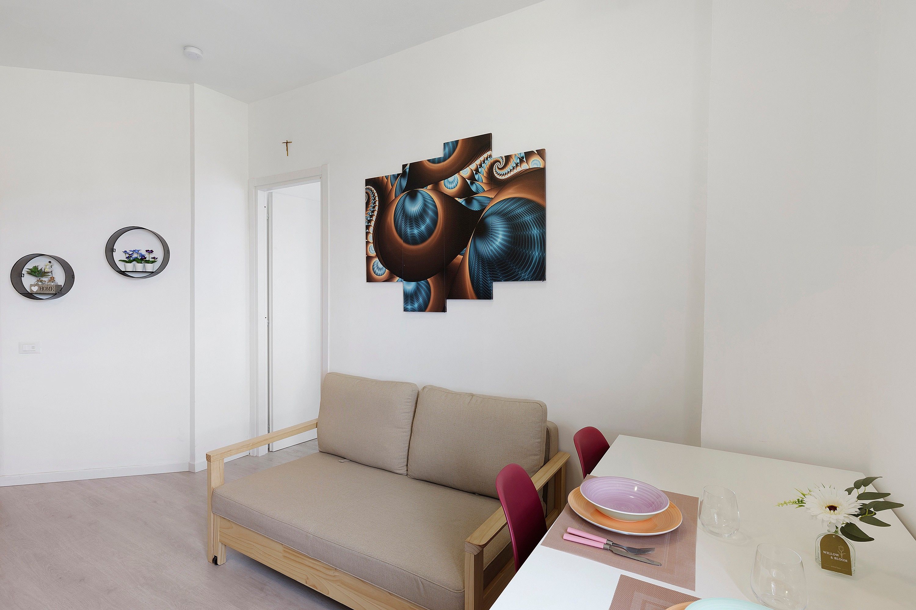 A minimalist living room with a sofa, a dining table with a vase of flowers, and abstract wall art.