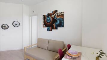 A minimalist living room with a sofa, a dining table with a vase of flowers, and abstract wall art.