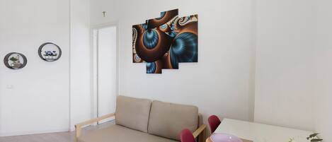 A minimalist living room with a sofa, a dining table with a vase of flowers, and abstract wall art.