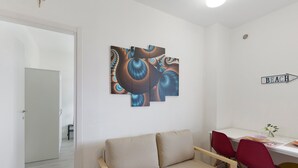 A modern living room with a sofa, a dining table with chairs, and a wall-mounted abstract art piece. - Vacation Home 'Appartamento A Costarainera' with Sea View, Wi-Fi, and Air Conditioning (Pantai)